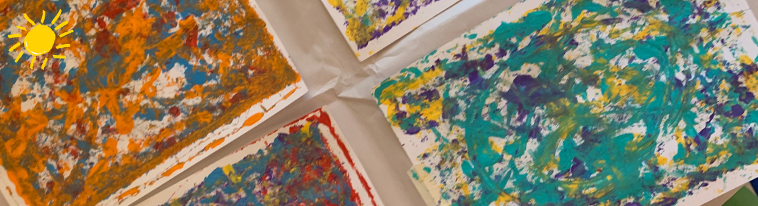 Children's abstract artwork, in shades of green and orange, sit on the table